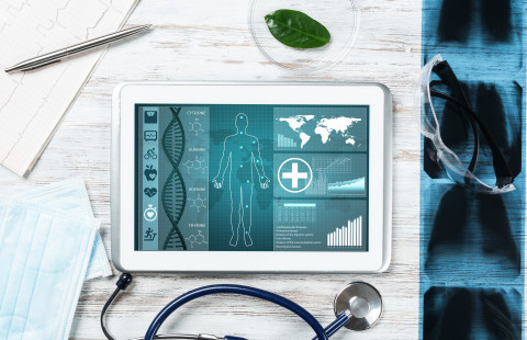 Tabletti näyttää ihmisen siluetin ja terveystiedon graafeja, ympärillä stetoskooppi, maski ja röntgenkuvia