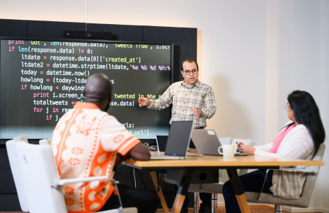 Man teaching two students in front of a screen