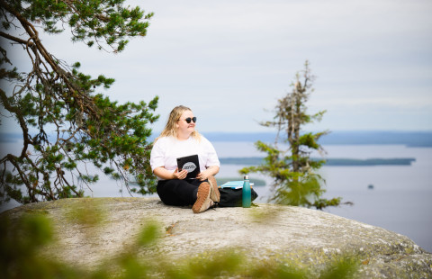 A young woman looks at her tablet on a high cliff on a summer day.