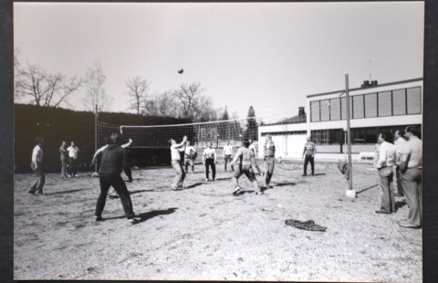 Miehiä pelaamassa lentopalloa ulkona hiekkakentällä.