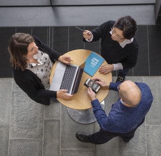 Kolme henkilöä neuvottelee pöydän ympärillä.