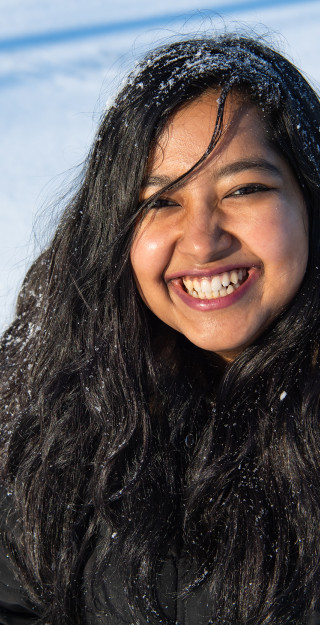 Young woman with dark hear and big smile with snow on her hair; picture taken outside, only snow on the background.