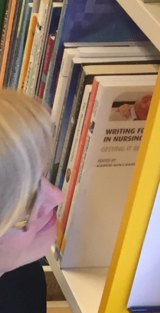 Kirjaston työtekijä osoittaa hyllynpäätykylttiä, jossa lukee aakkosvälitieto pro-äly.