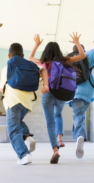 koululaiset juoksevat koulun käytävällä reput selässä