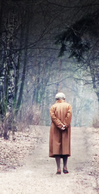 Vanha nainen kävelee metsätiellä.
