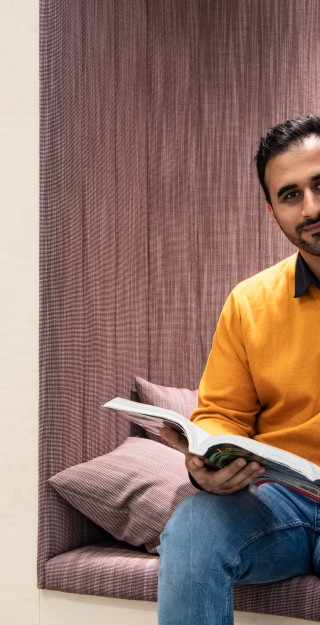 Dark haired with an orange shirt sitting and and holding a book