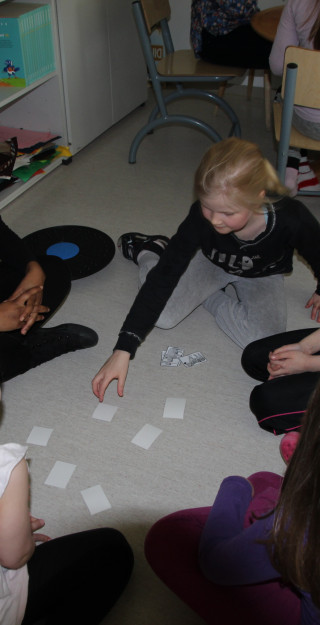 Opettaja ja oppilaita lattialla pelaamassa korttia.