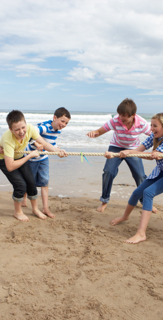Pojat ja tytöt kisaavat rannalla köydenvedossa.